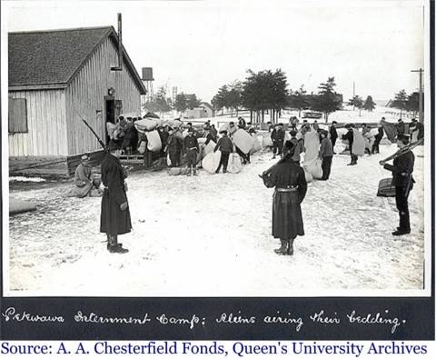 Photograph of internees carrying their beds into the crowded barracks where they slept at the Petawawa Internment Camp during WWI.